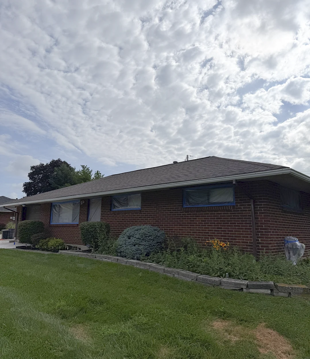 Brick home before exterior painting, windows taped for prep